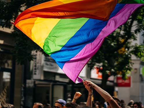 Hands holding a pride flag up with the flag waving against the sky
