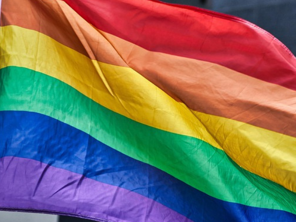 Hands holding a pride flag up with the flag waving against the sky